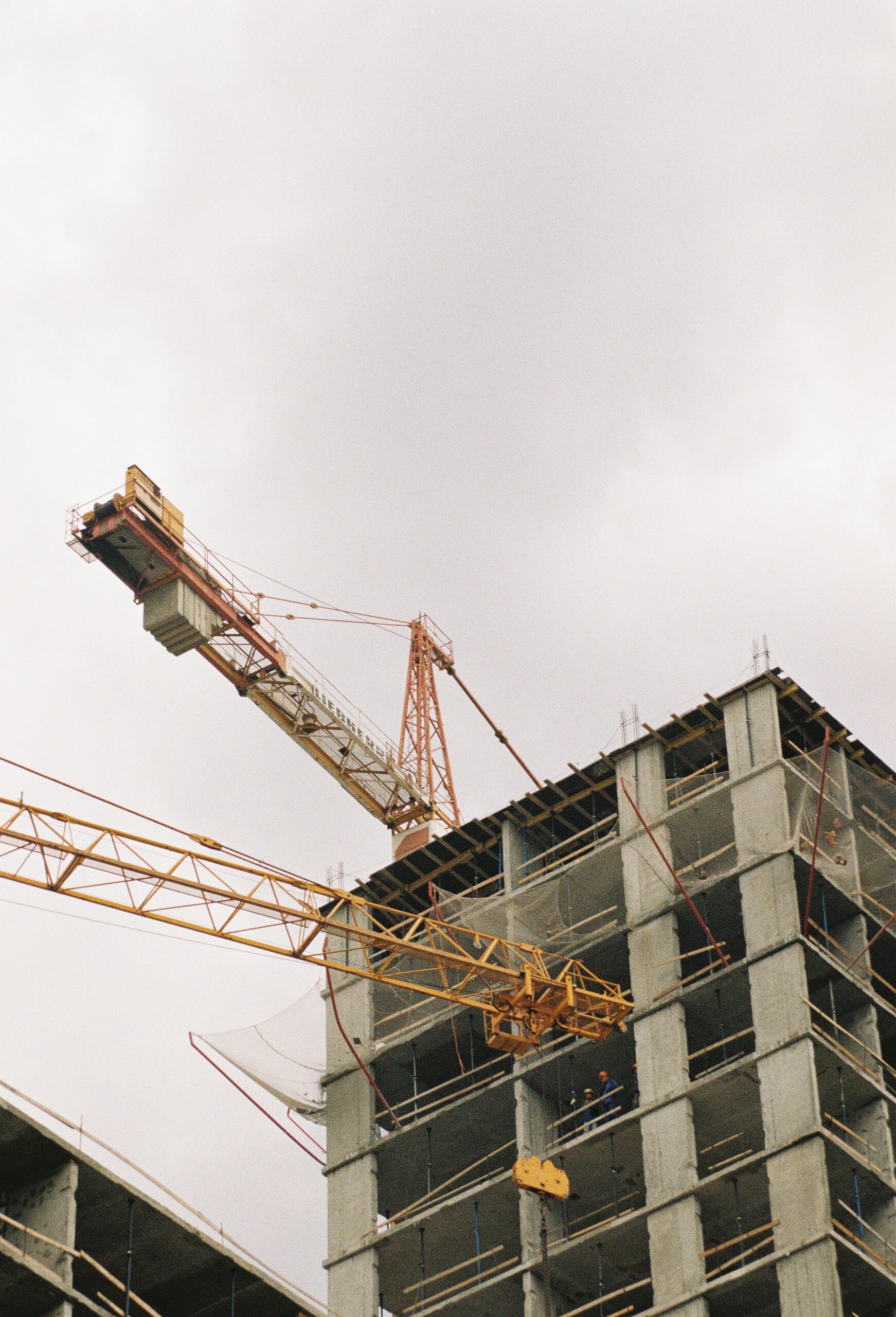 A high-rise building under construction with visible tower cranes and concrete structure.